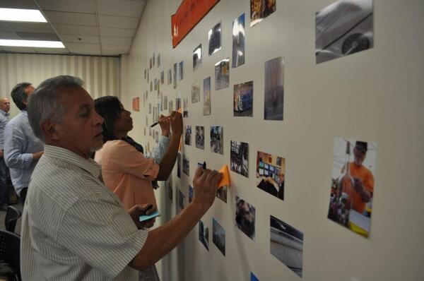 people writing on sticky notes on wall of photographs
